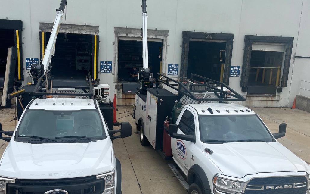 Two Kodiak utility trucks equipped with aerial lifts parked outside a warehouse.